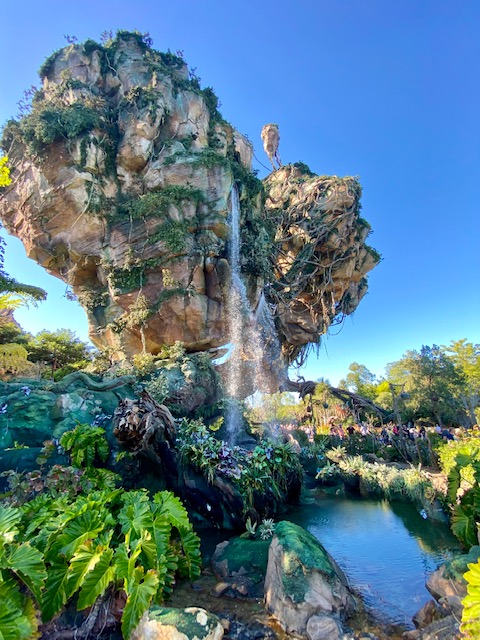 A scene from Animal Kingdom park at Walt Disney World, in Avatar world. Blue skies frame a huge rock formation with a waterfall. 