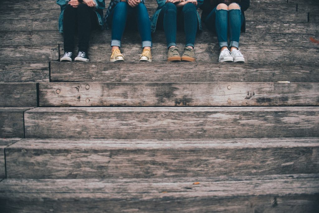 Four people sitting on wooden stairs each with different jeans and shoes. 