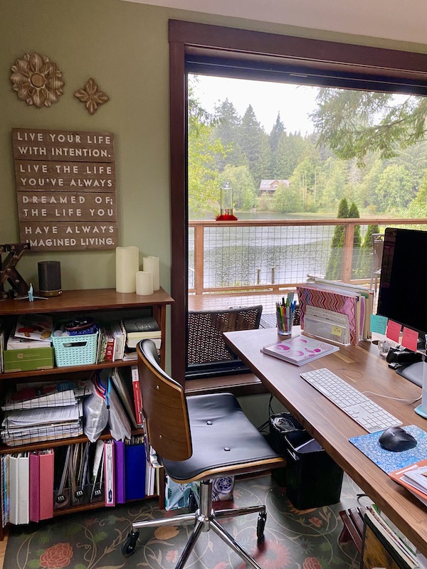 A desk and bookshelf in front of a window on a rainy day.