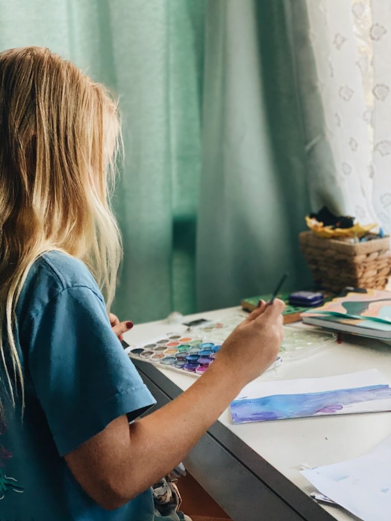 a girl in a blue shirt painting with watercolors.
