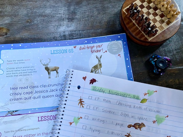A spiral notebook with homeschool tasks written in a list, a notebook with typing curriculum, a small chess set and a fidget spinner.