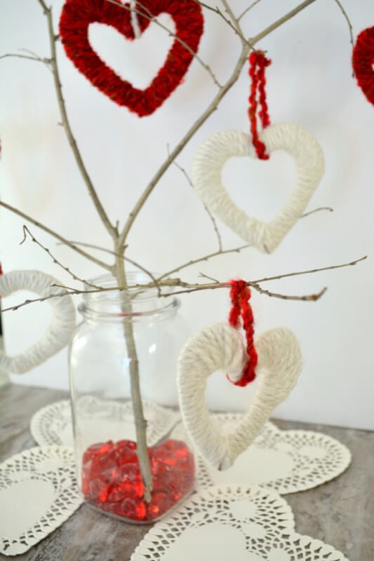 A branch in a jar on a table, with red and white yarn hearts hanging from the branches.