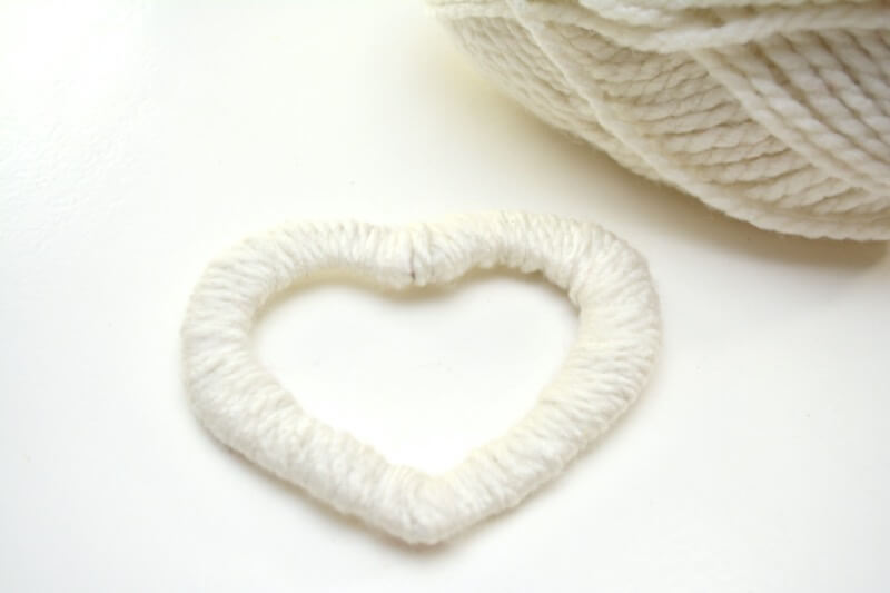 A cardboard heart wrapped in thick white yarn.